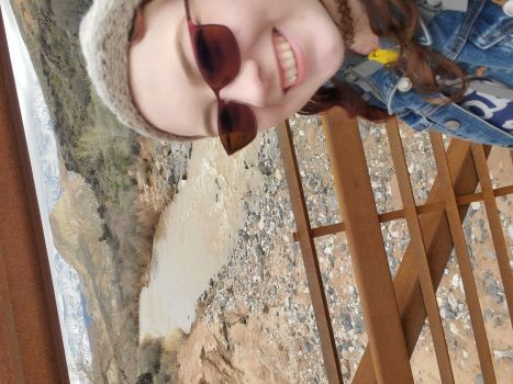 A girl with Red hair and glasses in on a bridge near the river